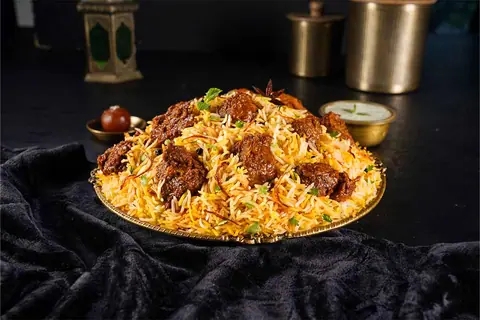 Plate of biryani with pieces of spiced meat and garnished with herbs
