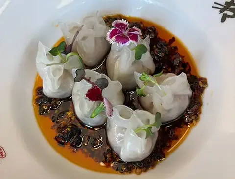 Steamed dumplings in spicy chili oil garnished with microgreens and edible flowers
