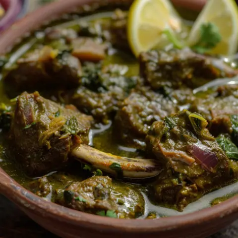Spicy mutton curry garnished with lemon wedges and herbs in a clay bowl