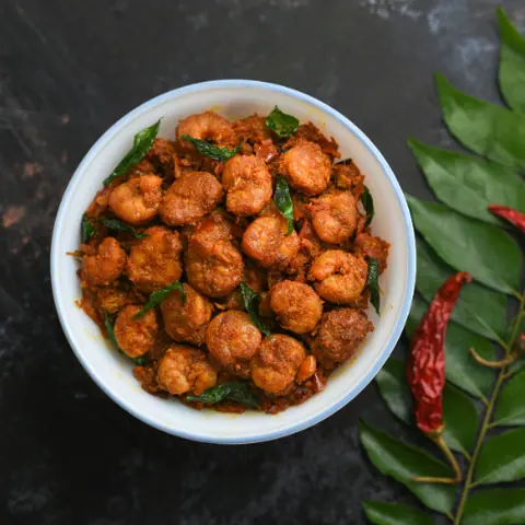 Spicy prawn fry garnished with curry leaves in a white bowl