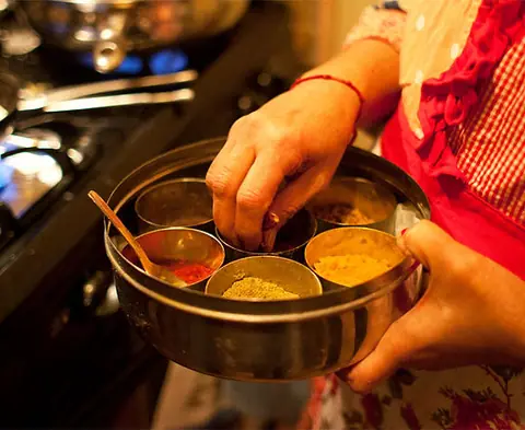 Hand holding a steel container with Indian spices near a stove