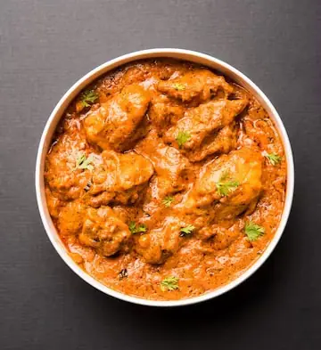 Chicken curry garnished with coriander in a white bowl
