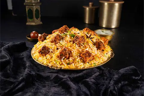 Plate of chicken biryani with spices and herbs on a brass plate