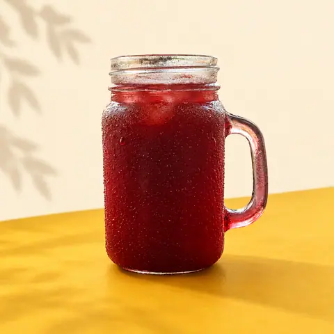 Iced red beverage in a glass jar with handle on yellow surface