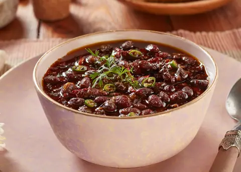 Bowl of spicy black chickpea curry garnished with green chilies and coriander