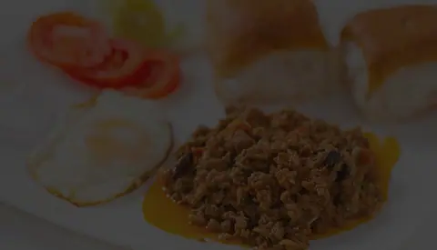 Keema pav with fried eggs and sliced tomatoes on a white plate