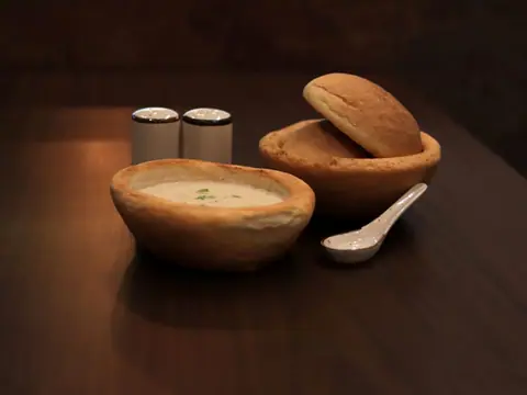 Bowl of creamy soup with two bread rolls and a spoon on wooden table