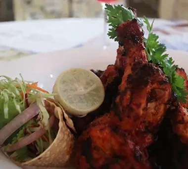 Tandoori chicken drumsticks with lemon and salad on a white plate