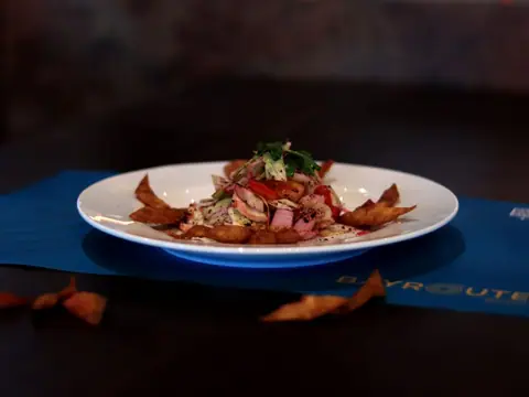 Garnished dish with sliced meat and crispy chips on a white plate