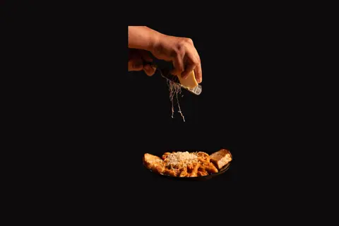 Hand grating cheese over a plate of pasta