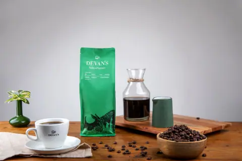 Cup of black coffee with Devan's branded coffee bag and coffee beans