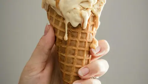 Hand holding a melting ice cream cone with creamy vanilla ice cream