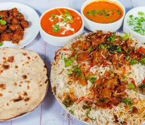 Plate of biryani with roti and three bowls of curry and raita