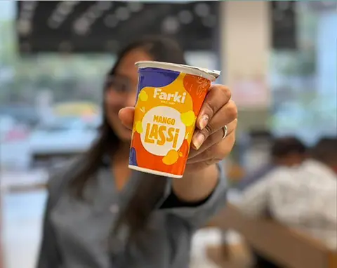 Hand holding a cup of Farki mango lassi drink