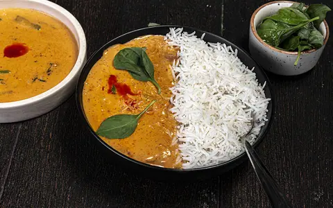 Bowl of curry with white rice and fresh spinach leaves on black surface