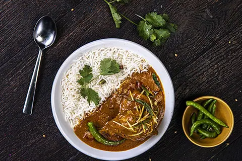 Plate of white rice with curry garnished with green chili and coriander