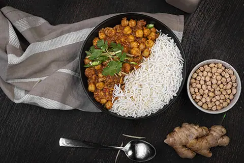 Chickpea curry with white rice served in a black bowl with ginger and raw chickpeas