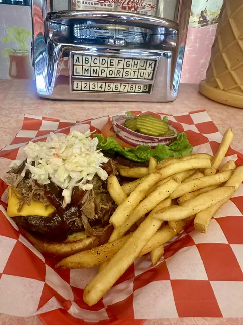 Cheeseburger with pulled pork, coleslaw, lettuce, pickles, onions, and French fries