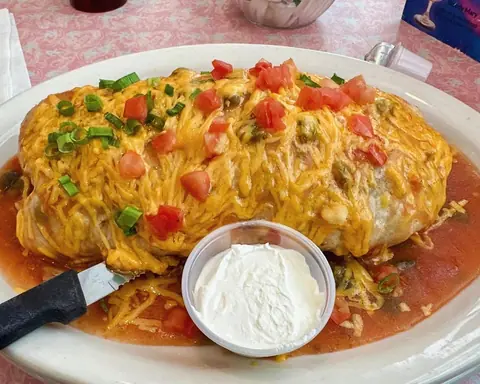Cheese-covered burrito topped with diced tomatoes and green onions, with sour cream