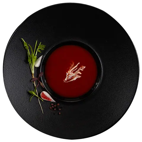 Red soup with cream swirl and herbs on black plate