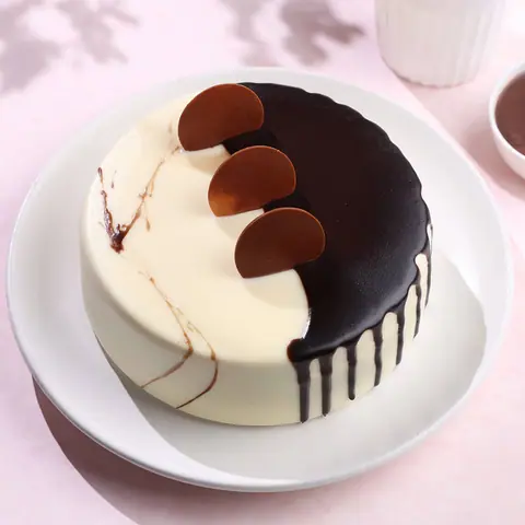 Round cake with half white and half dark chocolate glaze topped with chocolate discs
