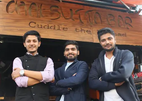 Three men standing outside Chai Sutta Bar with wooden signboard