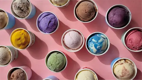 Multiple scoops of colorful ice cream in cups on a pink surface