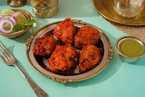 Plate of spicy fried chicken pieces with green chutney and onion salad