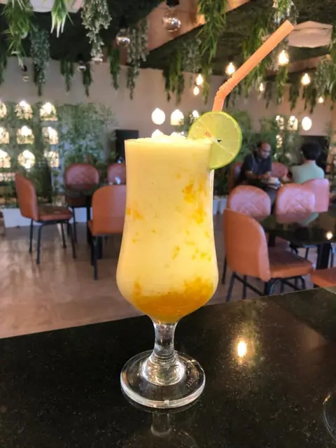 Mango smoothie garnished with lime slice and straw in cafe interior