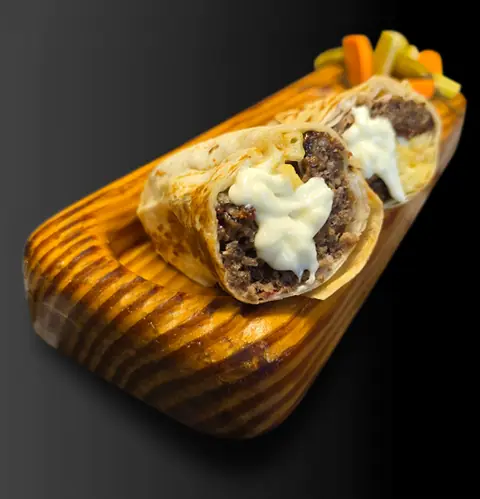 Middle-eastern wrap with minced meat and white sauce on wooden board