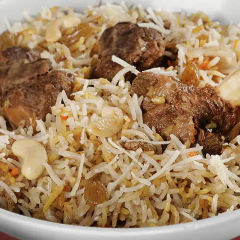 Bowl of biryani with pieces of meat, cashews, and raisins
