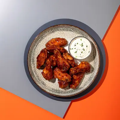 Plate of spicy chicken wings with a side of white dipping sauce