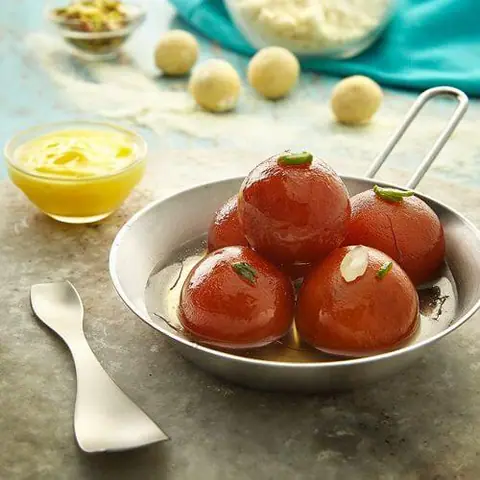Gulab jamun served in a small pan with saffron custard on the side