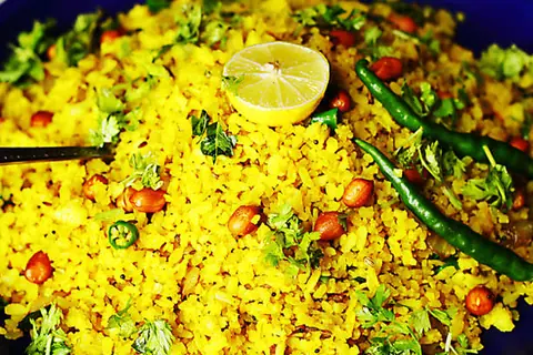 Spiced poha garnished with peanuts, green chilies, coriander, and lemon half